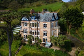 A large, multi-story building with a prominent tower, surrounded by lush greenery and a well-maintained garden. - Finest Retreats | Westwell Hall (Ilfracombe)