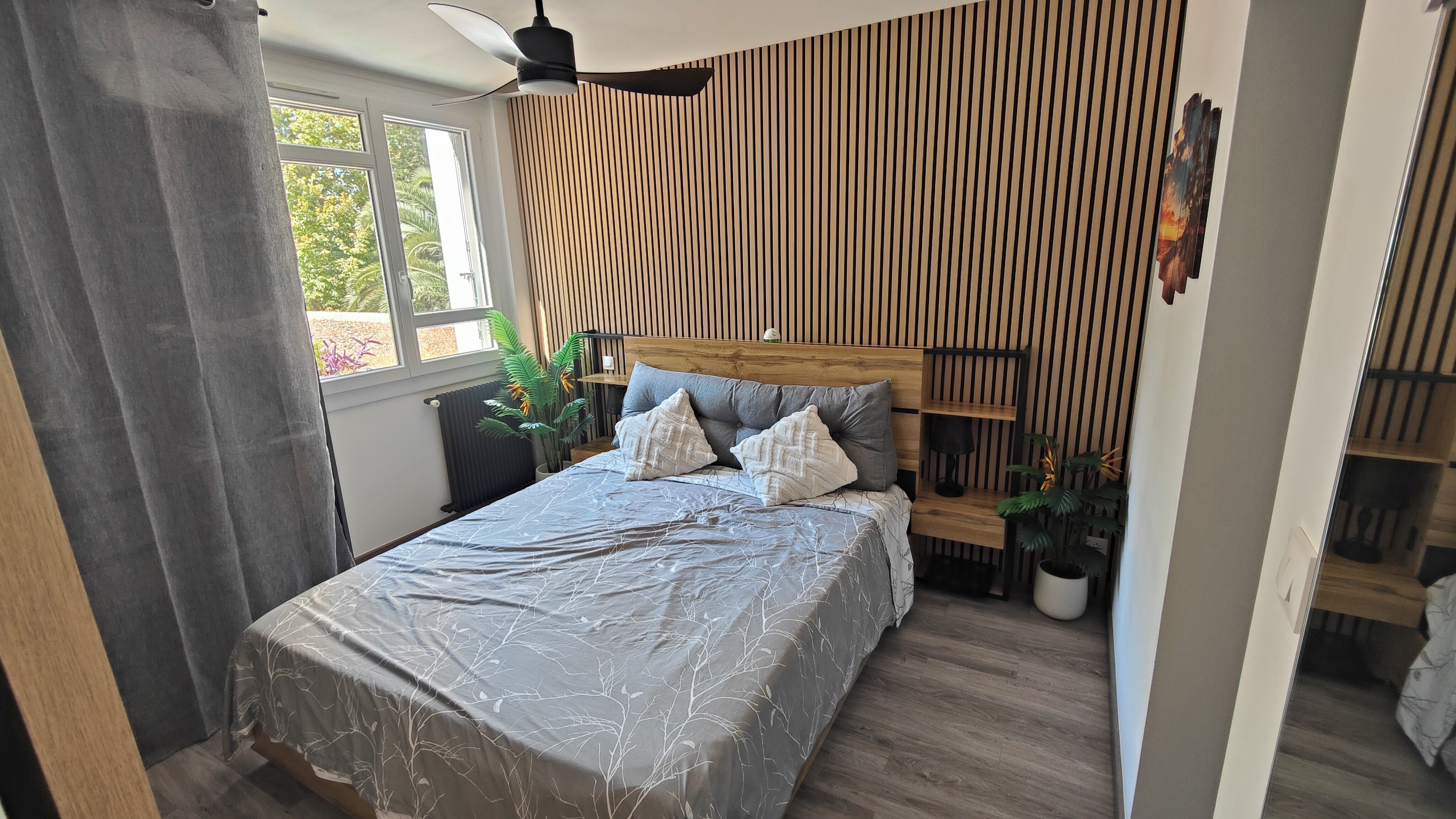 Un dormitorio con cama, ventilador de techo, ventana y radiador.