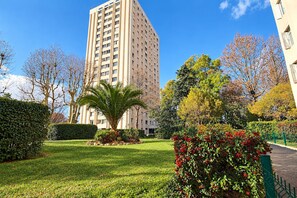 A tall building with a modern design, surrounded by well-maintained greenery and trees.