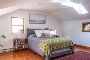 A bedroom with a sloped ceiling, a bed with a green patterned bedspread, a bookshelf, two bedside lamps, and a framed picture on the wall. - LIBRARY HOUSE IN THE WOODS NEAR CHATHAM (Chatham)