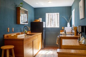 A compact kitchen with wooden cabinetry, a built-in sink, and a window providing natural light. - LIBRARY HOUSE IN THE WOODS NEAR CHATHAM (Chatham)
