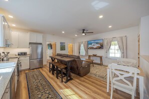 Una cocina moderna con armarios blancos, un refrigerador de acero inoxidable y un comedor con sofá de cuero marrón y mesa de madera.
