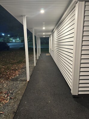 Un pasillo cubierto con piso oscuro que conduce a un edificio con revestimiento blanco.