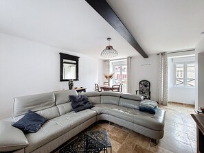 A modern living room with a curved sofa, a dining table, and a chandelier. - Renovated stone house, 3 bedrooms (Montsenelle)