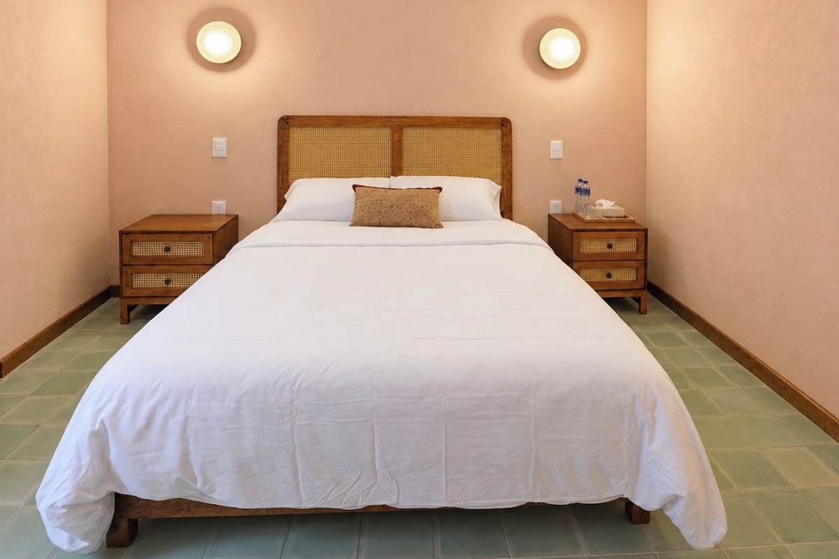Un grand lit avec une tête de lit en bois, deux tables de chevet avec des paniers en osier et des lampes fixées au mur.
