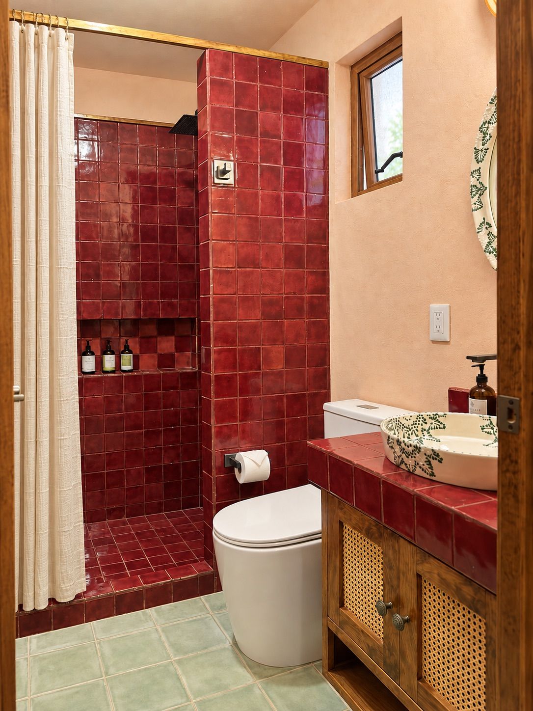 Une salle de bain avec des murs recouverts de carreaux rouges, des toilettes blanches, un meuble-lavabo en bois avec un évier et un espace douche.