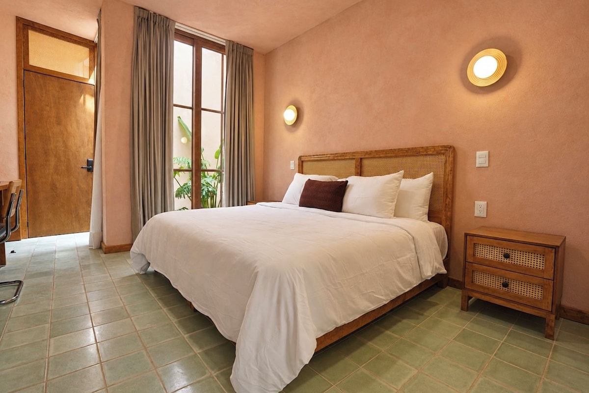 Une chambre à coucher avec un grand lit, une table de chevet et une fenêtre avec des rideaux.