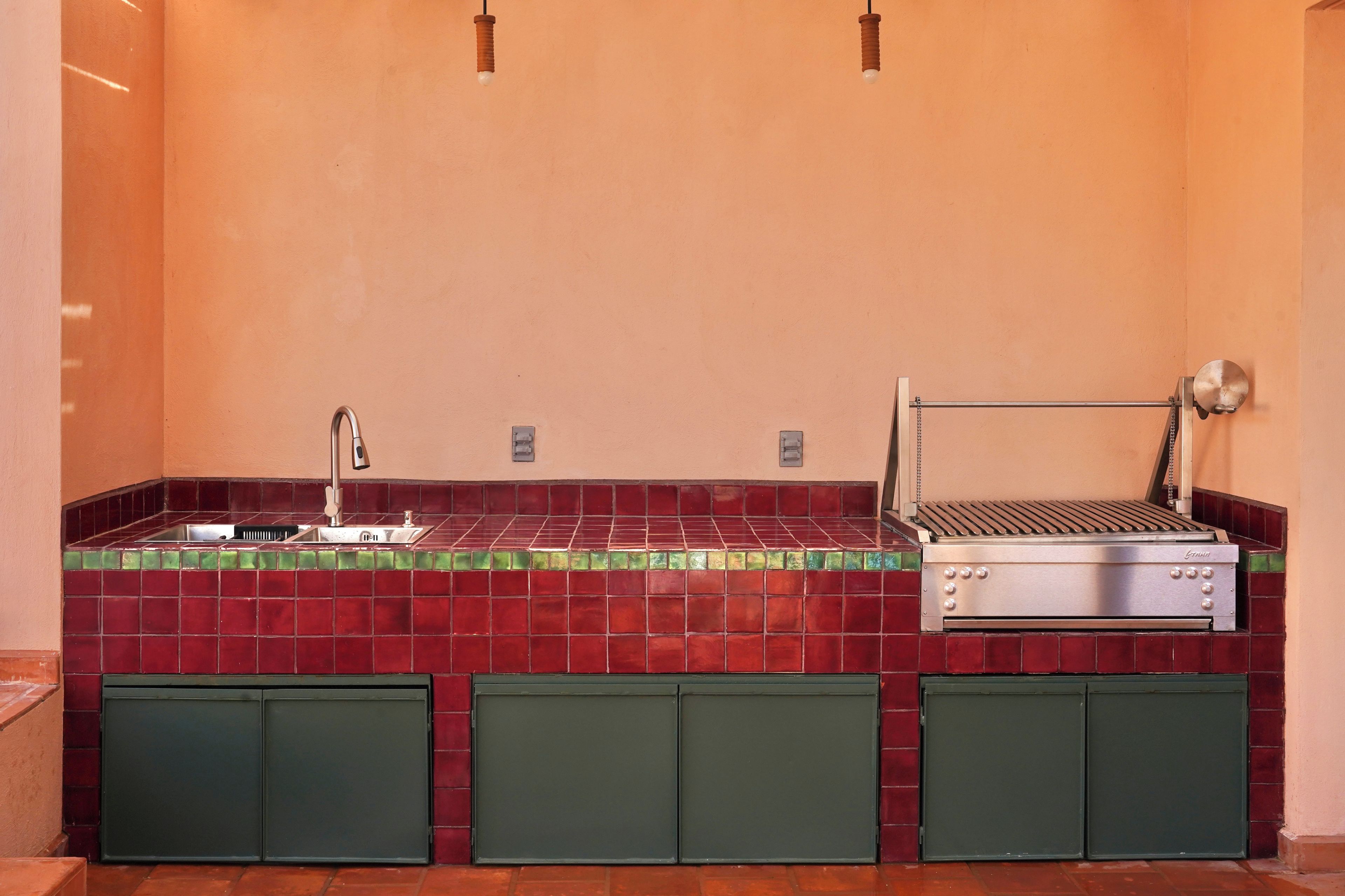 Une cuisine équipée d’un évier, d’un barbecue et de meubles de couleur verte.