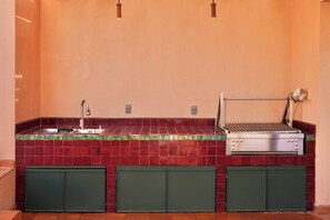 Une cuisine équipée d’un évier, d’un barbecue et de meubles de couleur verte.