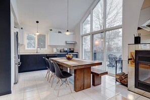 A modern kitchen with a large island, black chairs, and a dining table. - Le Havre | Private Hot Tub | Hammock & Lake (Mansonville)