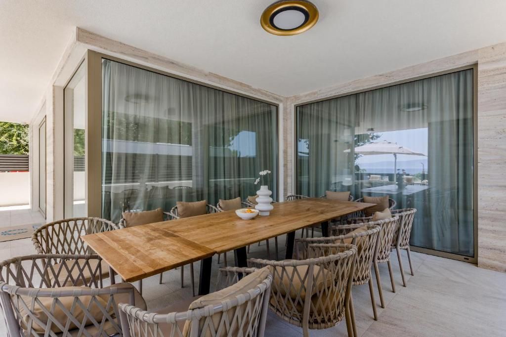 A dining area with a wooden table and wicker chairs, large glass windows, and a view of the outdoors.