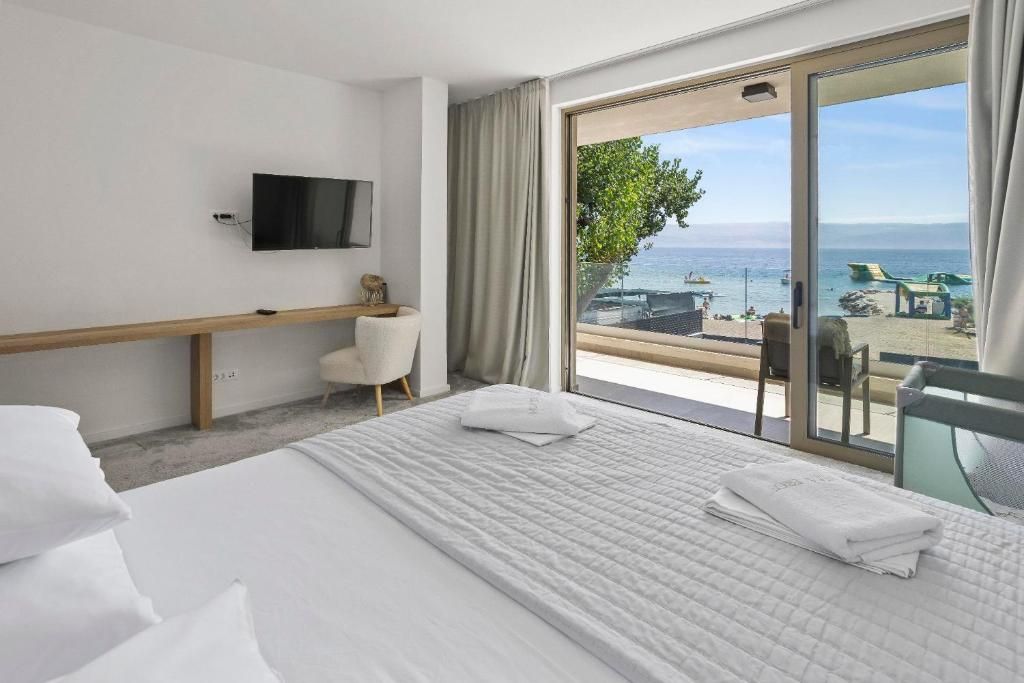 A hotel room with a bed, a TV, a desk, and a view of the sea.