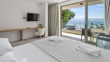 A hotel room with a bed, a TV, a desk, and a view of the sea.