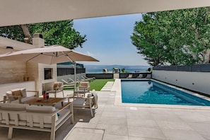 Zona de piscina exterior moderna con mobiliario y vistas al mar.