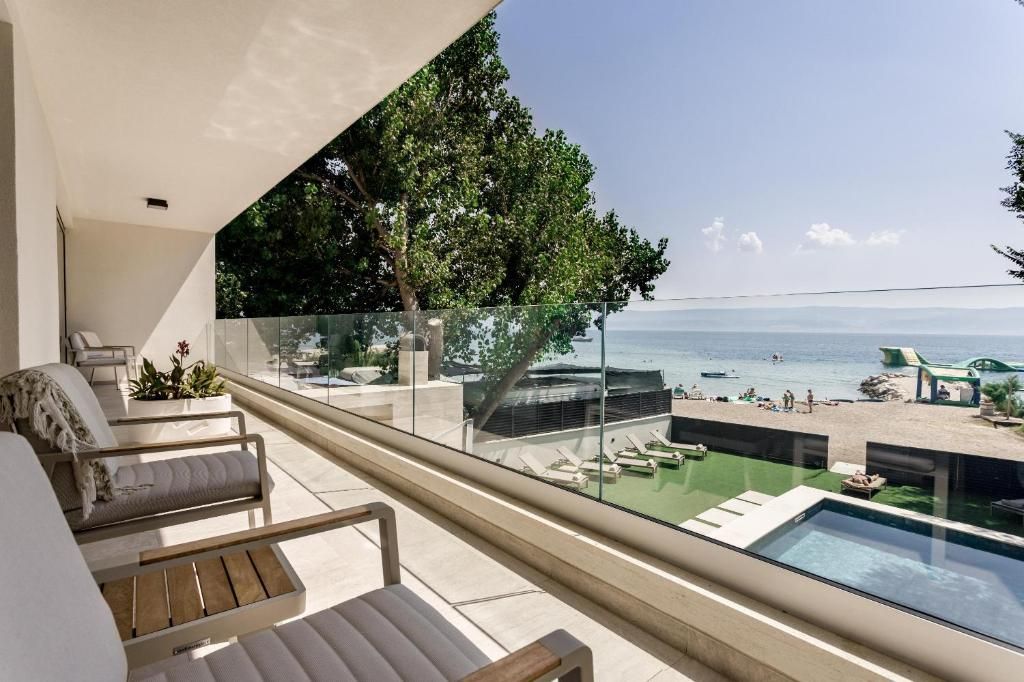 A balcony with a glass barrier, outdoor seating, a pool, and a view of the sea.