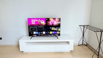 A flat-screen TV on a white stand in a room with a wooden floor and a metal drying rack.