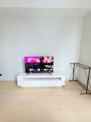 A flat-screen TV on a white stand in a room with a wooden floor and a metal drying rack. - Colony Infinitum Sky Pool KLCC (Kuala Lumpur)