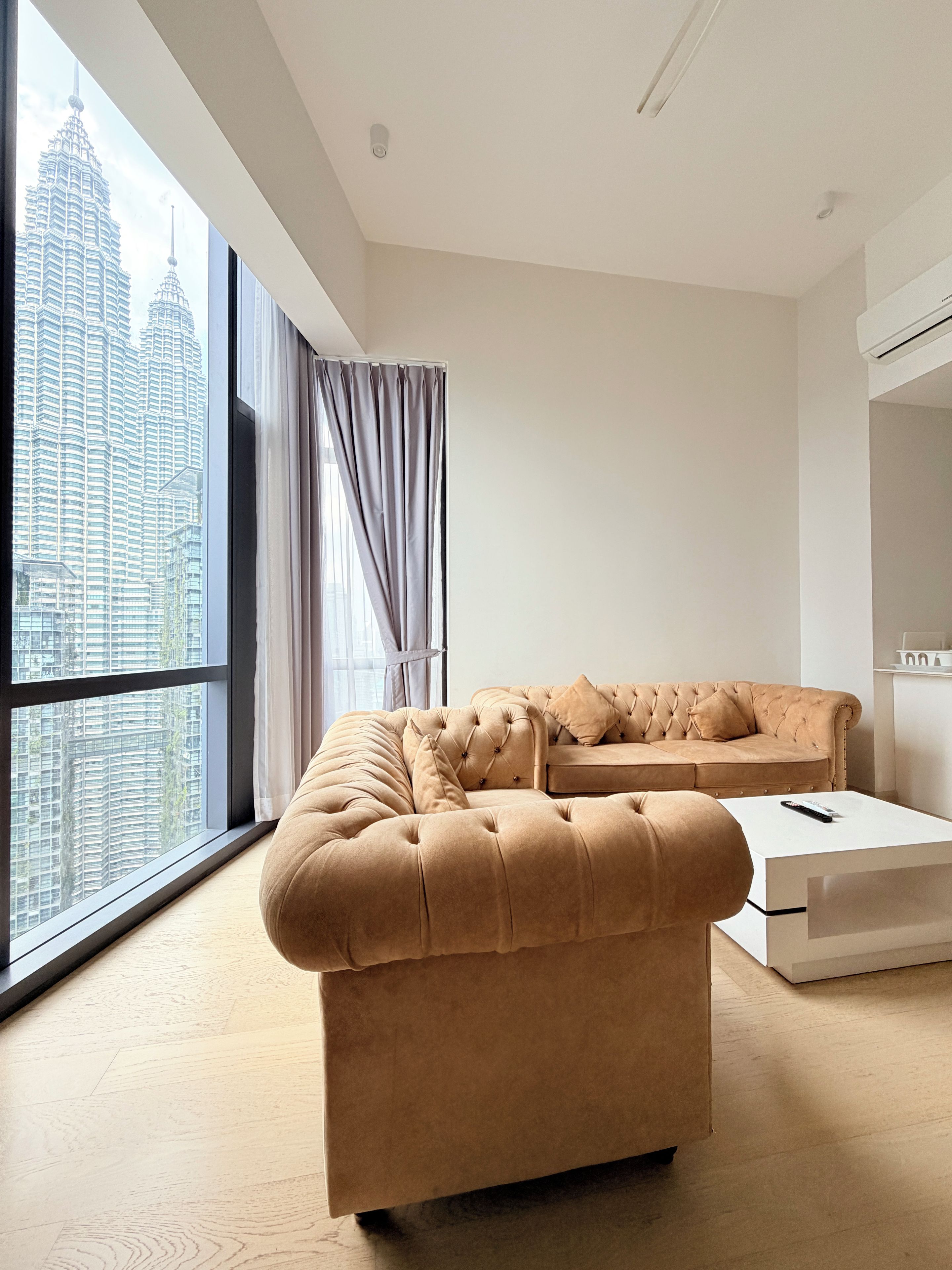Ein modernes Wohnzimmer mit großem Fenster, einem gesteppten Sofa und einem schlichten Couchtisch.