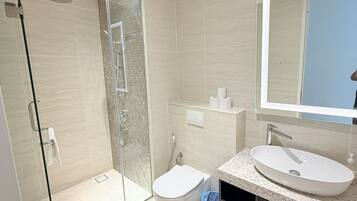A modern bathroom with a glass-enclosed shower, a toilet, and a sink with a large mirror above it.
