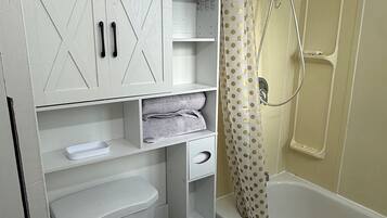 A bathroom with a toilet, a sink, a shower with a curtain, and a cabinet with storage space.