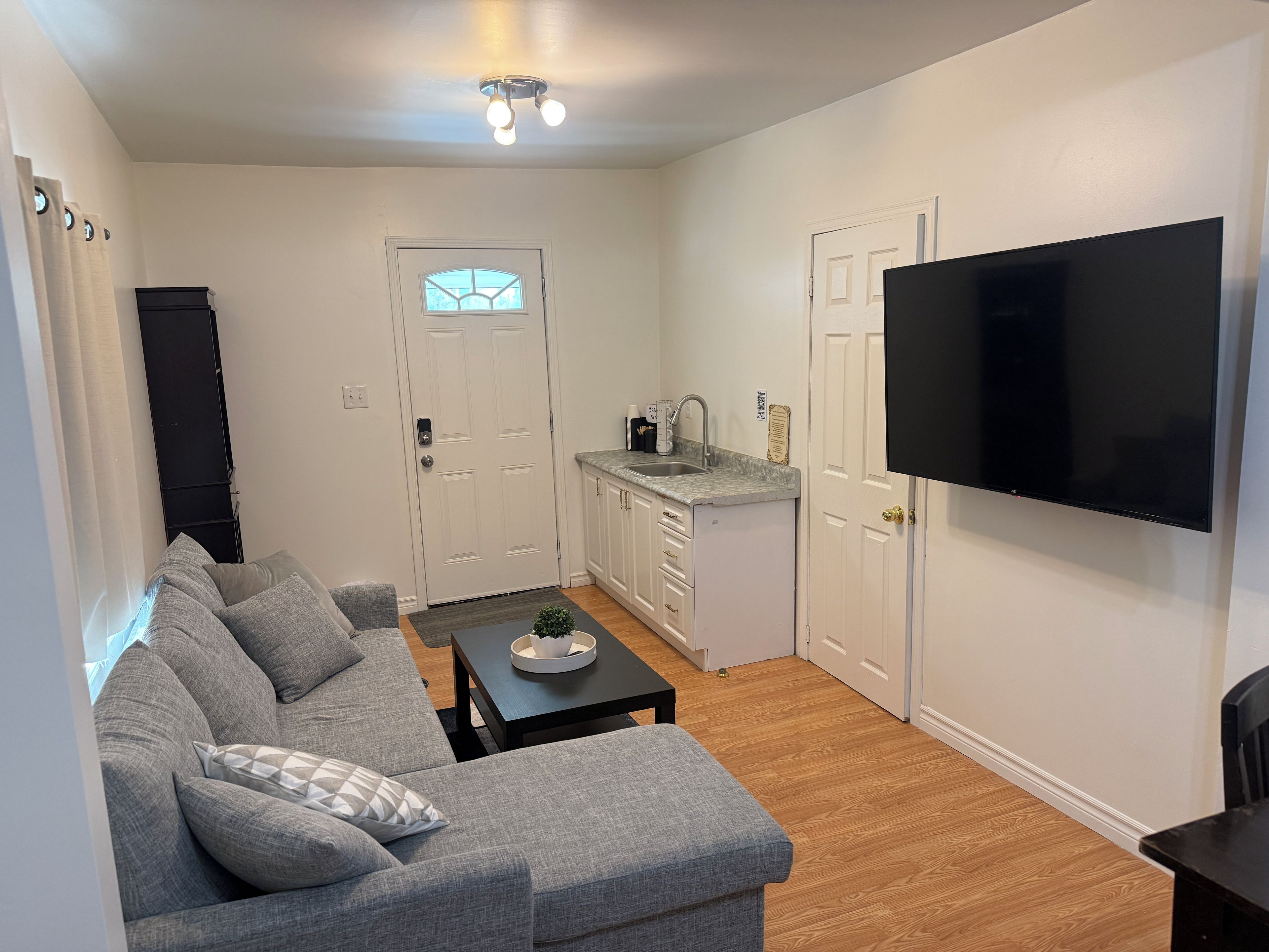 Ett modernt vardagsrum med en grå soffa, ett soffbord och en platt-TV som är monterad på väggen.