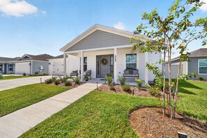 A modern single-story house with a covered porch, a front yard with a small tree, and a clear sky. - Charming Fenced Eastport Cottage with Golf Cart (Wildwood)
