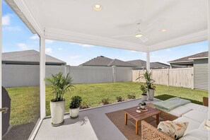A covered patio area with a seating arrangement, potted plants, and a view of a backyard. - Charming Fenced Eastport Cottage with Golf Cart (Wildwood)