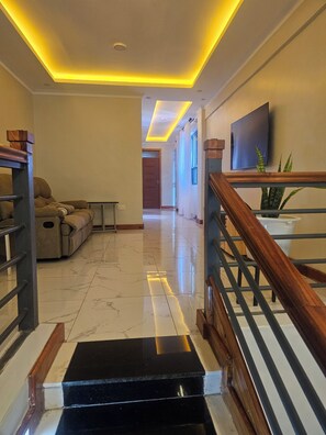 A hallway with a staircase, a sofa, a television, and a plant. - Serene 4-bedroom resort in welcoming Eldoret for your getaway (Eldoret)
