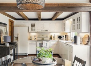 Una cocina moderna con muebles blancos, una isla central con una planta y un comedor con mesa de vidrio.