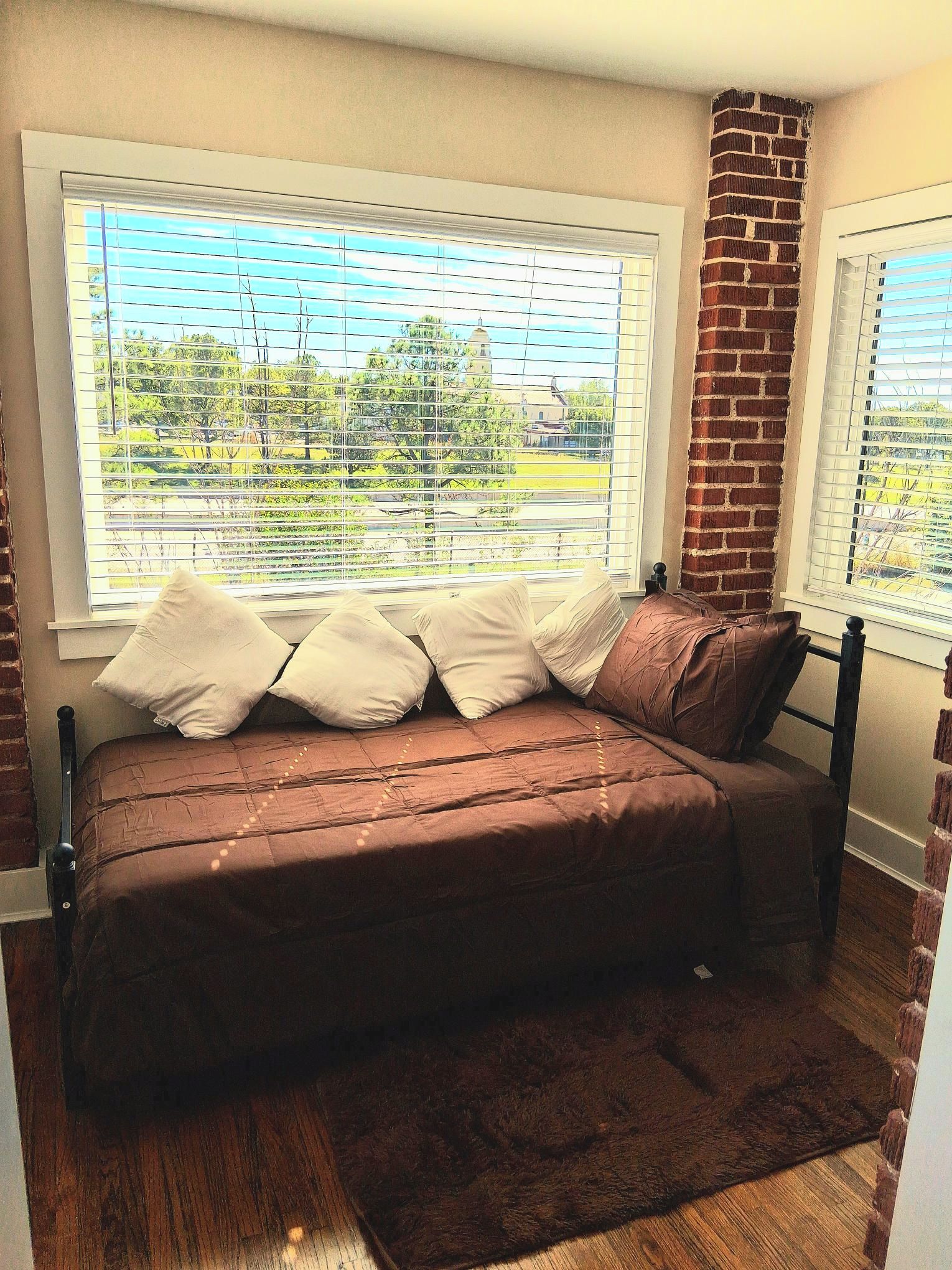 A bedroom with a bed, a window with blinds, and a brick wall.