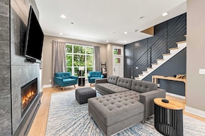A modern living room with a fireplace, a large sectional sofa, a television, and a staircase. - Westfield Landing | Walkable • Carmel • Designer (Westfield)