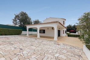 Un piccolo edificio bianco con tetto in tegole, un portico coperto e un ingresso con pavimento in pietra.