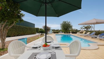Ett område vid poolen med ett bord för två, en pool och solstolar.