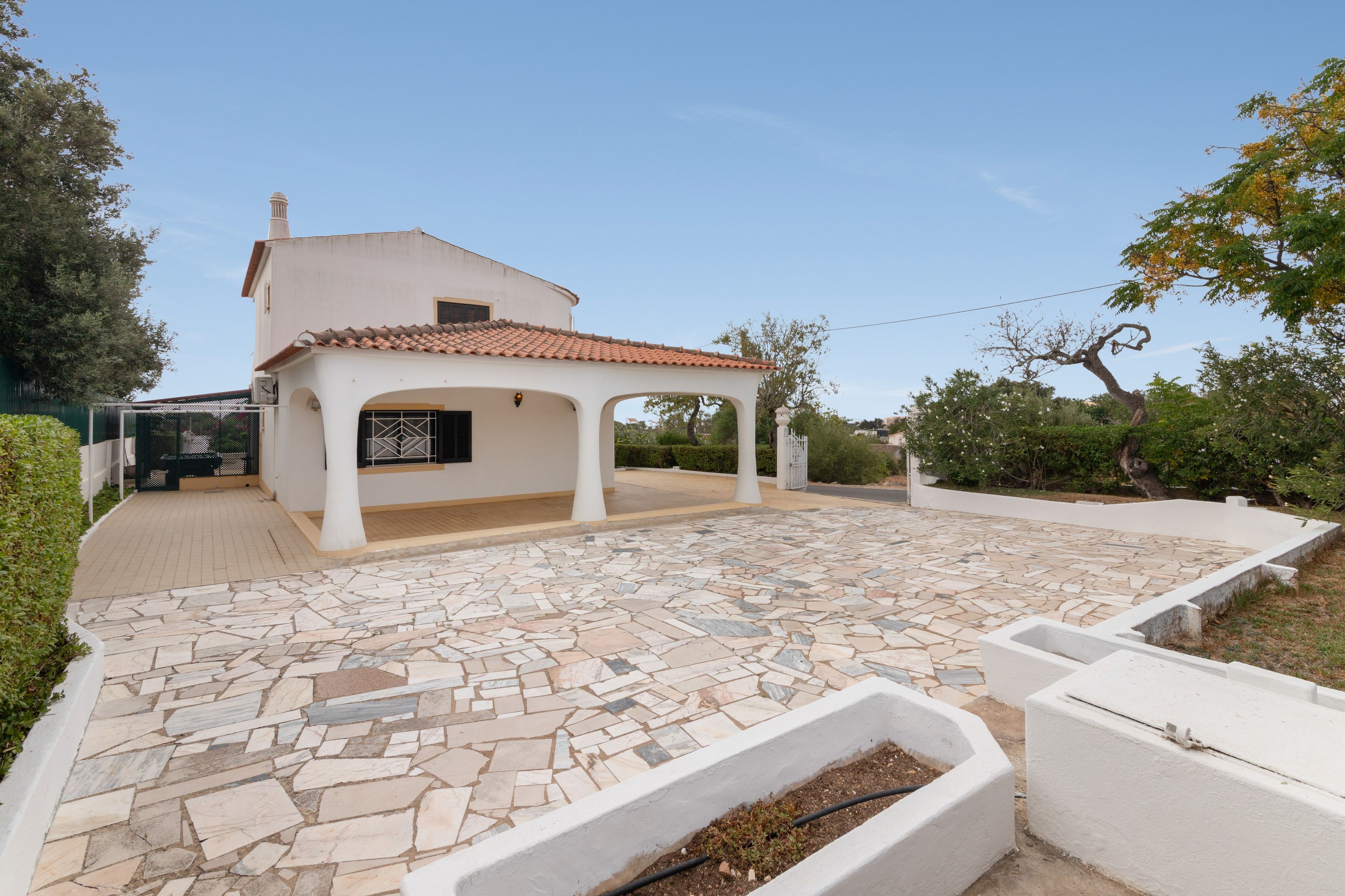Une maison dotée d’un patio carrelé, d’un espace extérieur aménagé et couvert, et d’un jardin agrémenté d’un jardinière murale blanche.