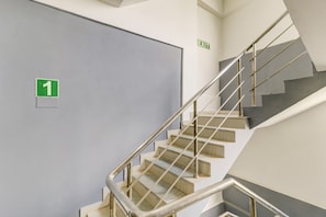 Una escalera con barandilla metálica y una puerta señalizada con un letrero verde de salida.