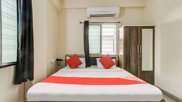 A hotel room with a bed, a wardrobe, an air conditioning unit, a window with curtains, and a bedside telephone.