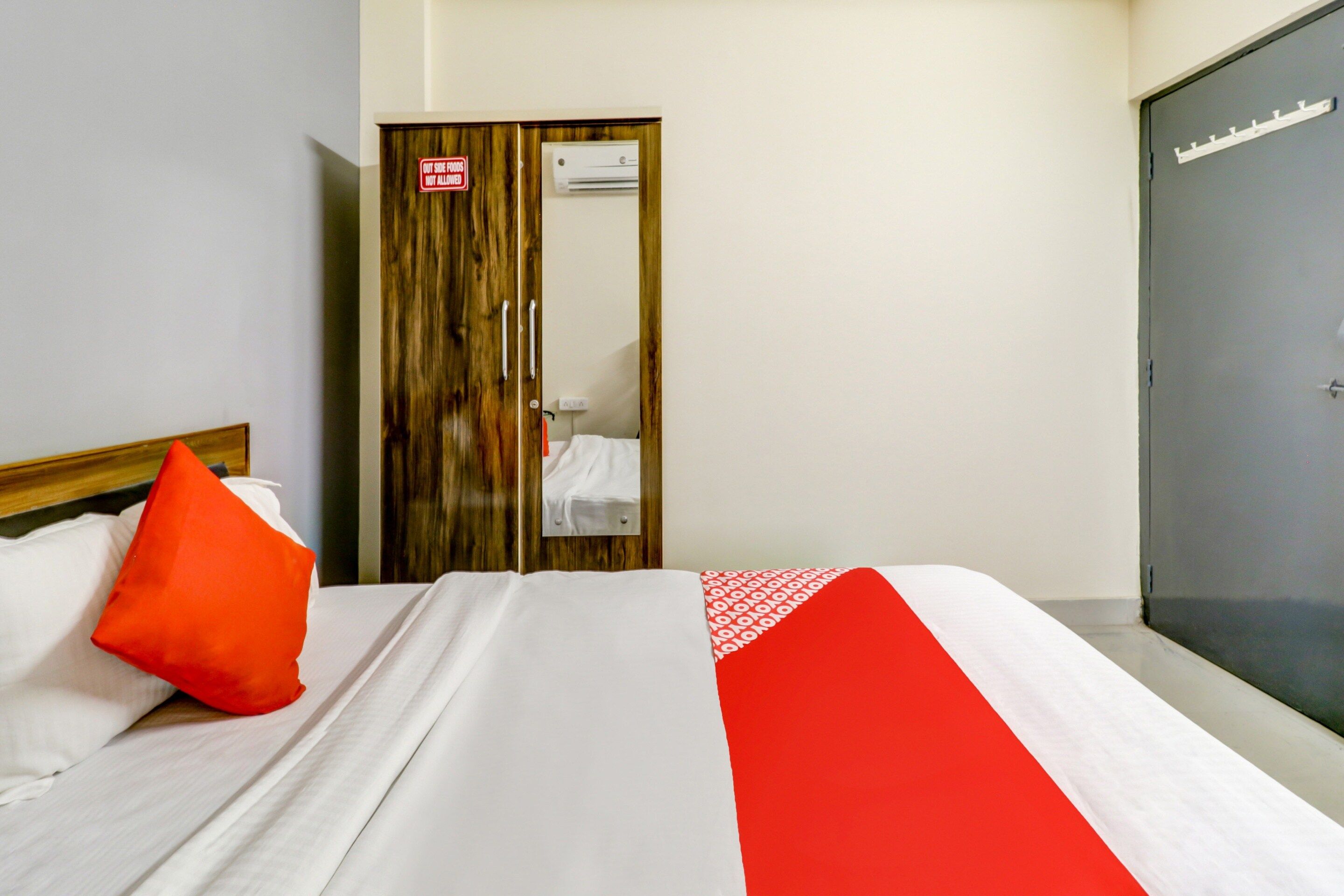 A hotel room with a bed, a red pillow, a wardrobe, and a door with a sign.