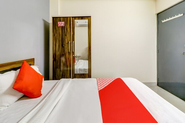 Una habitación de hotel con cama, almohada roja, armario y puerta con un cartel.