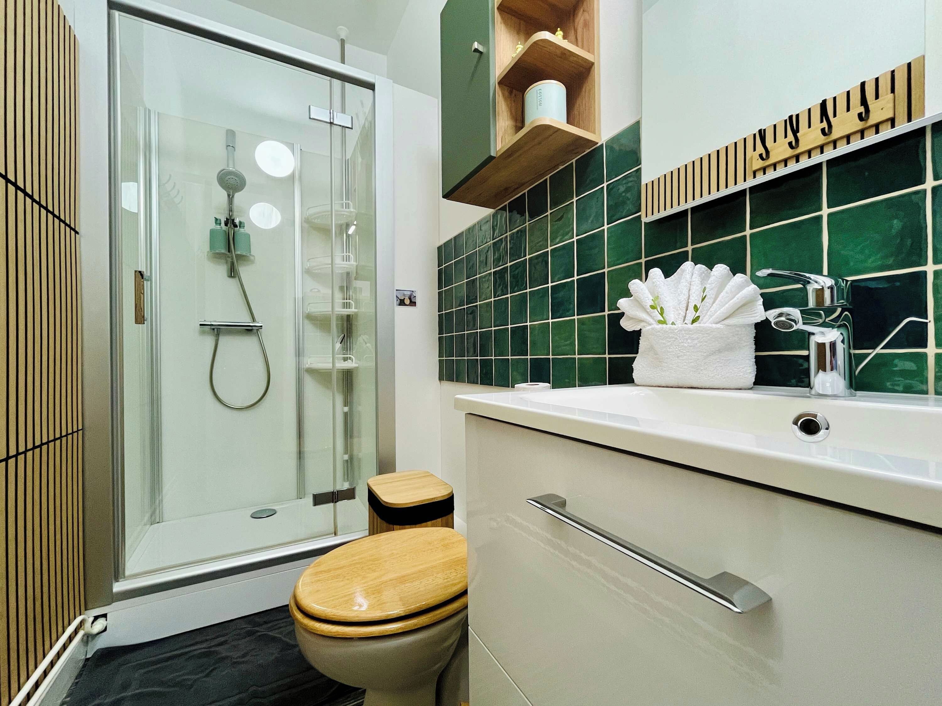 Een moderne badkamer met een glazen douchecabine, een houten toilet en een wastafel met spiegel en handdoekhouder.