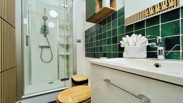 Een moderne badkamer met een glazen douchecabine, een houten toilet en een wastafel met spiegel en handdoekhouder.