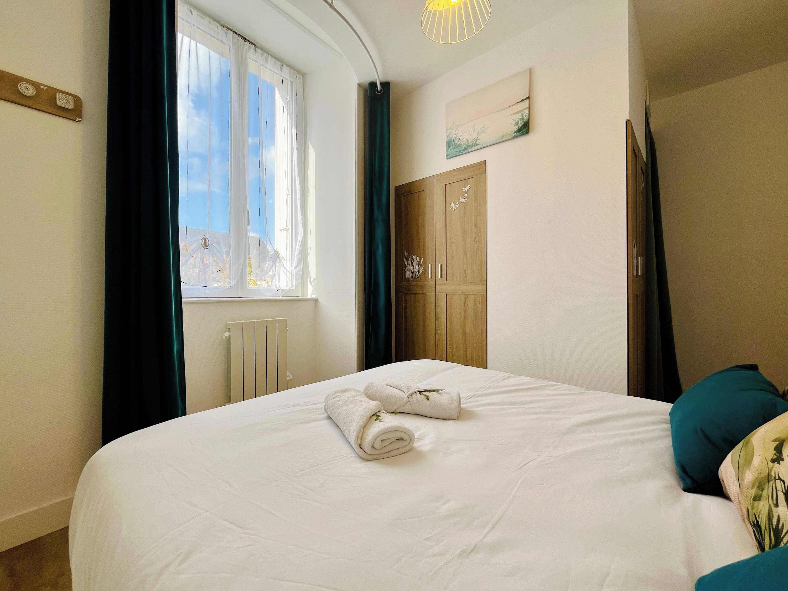 Une chambre à coucher avec un lit, une fenêtre avec des rideaux, un radiateur et une armoire en bois.