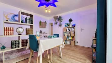 Een kamer met een plafondlamp in de vorm van een ster, een eettafel met stoelen en planken met boeken en decoratieve voorwerpen.