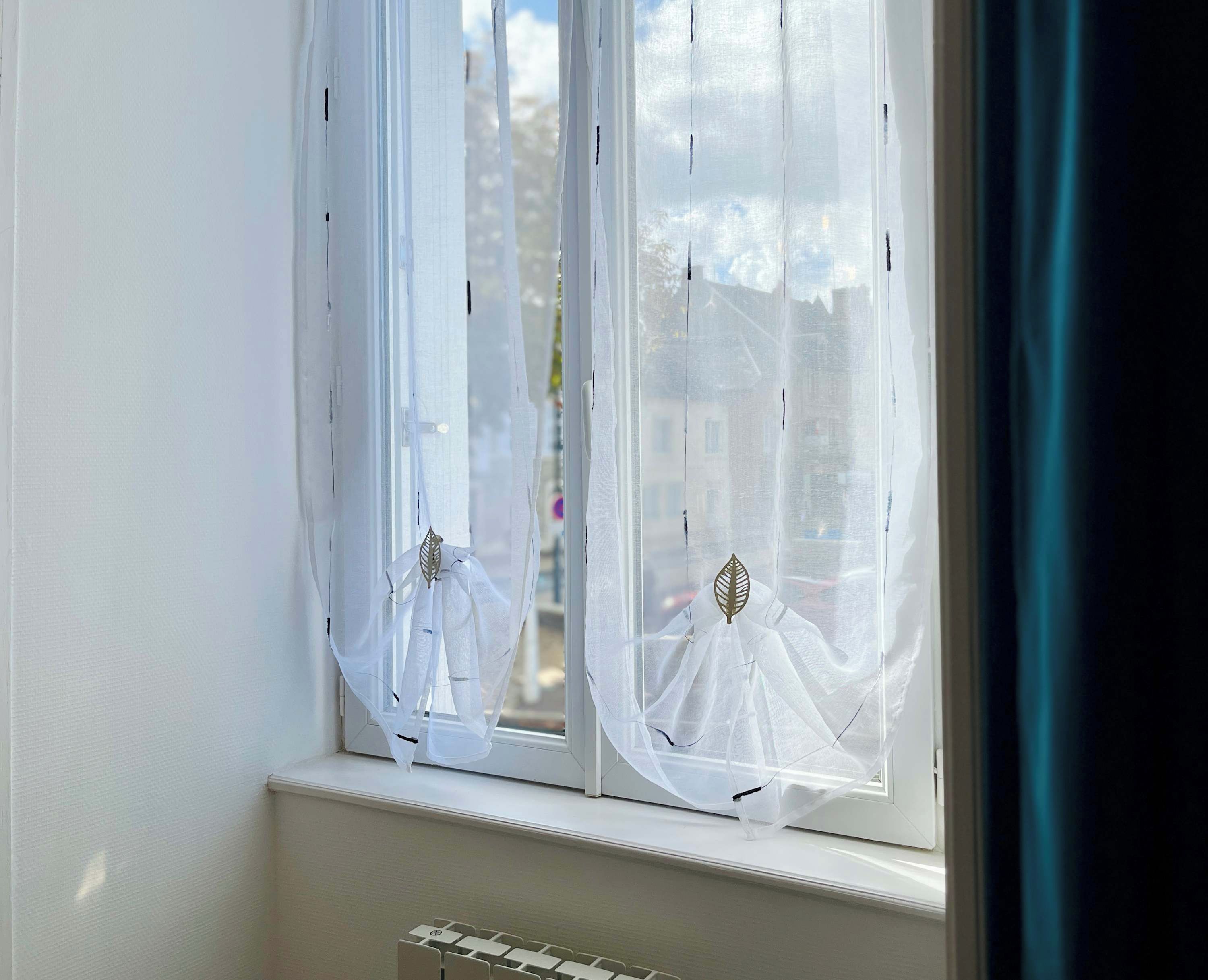 A window with white curtains and a leaf-shaped decoration.