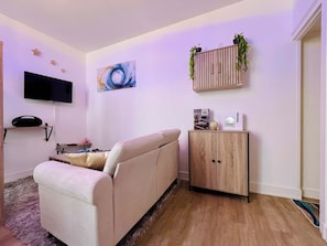 Ein Wohnzimmer mit einer Couch, einem Flachbildfernseher, einem Gemälde, einer Vitrine mit Pflanzen und einem Globus.