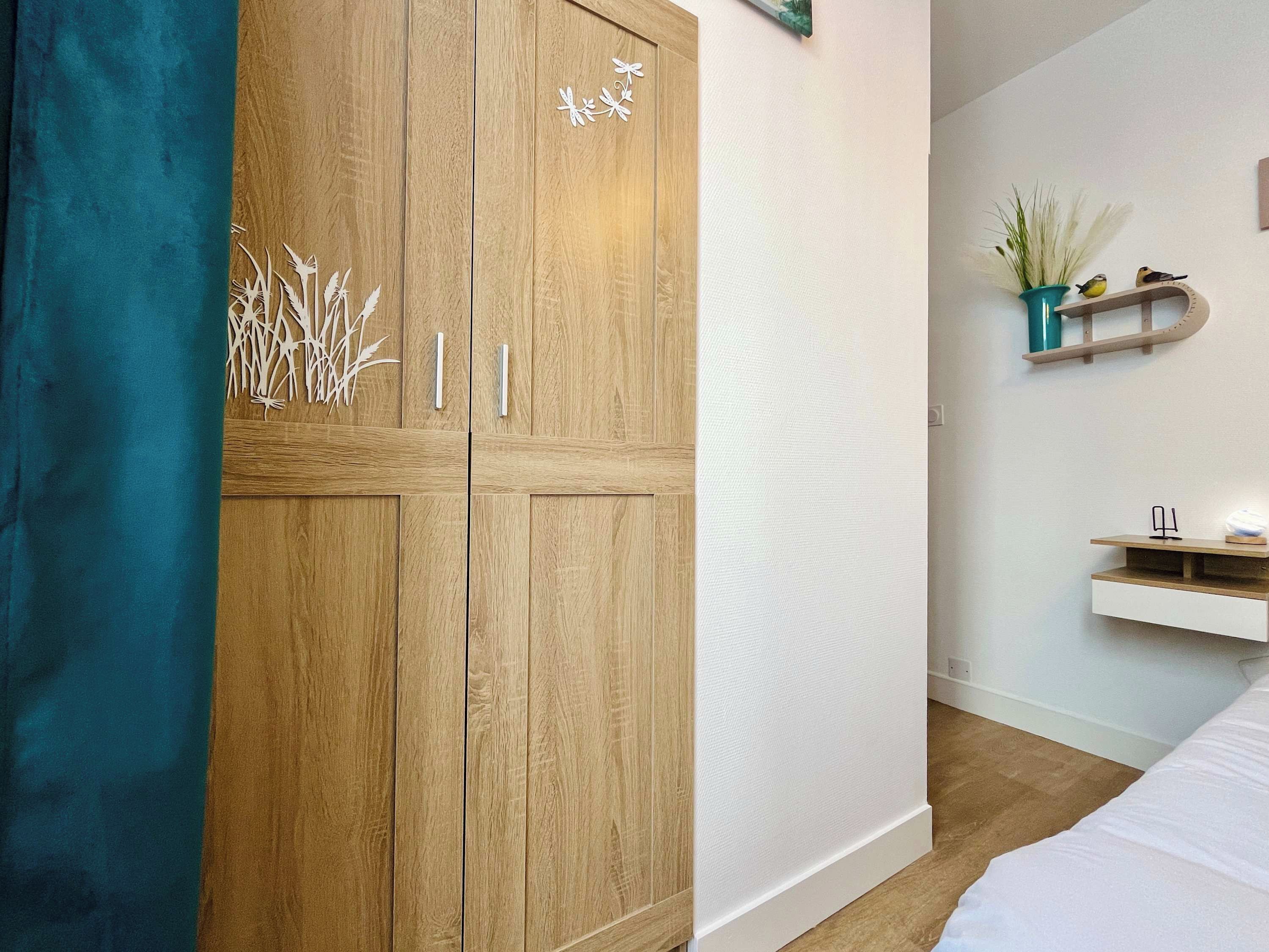 Une chambre à coucher avec une armoire en bois, un lit, un mur blanc et une étagère ornée d’objets décoratifs.