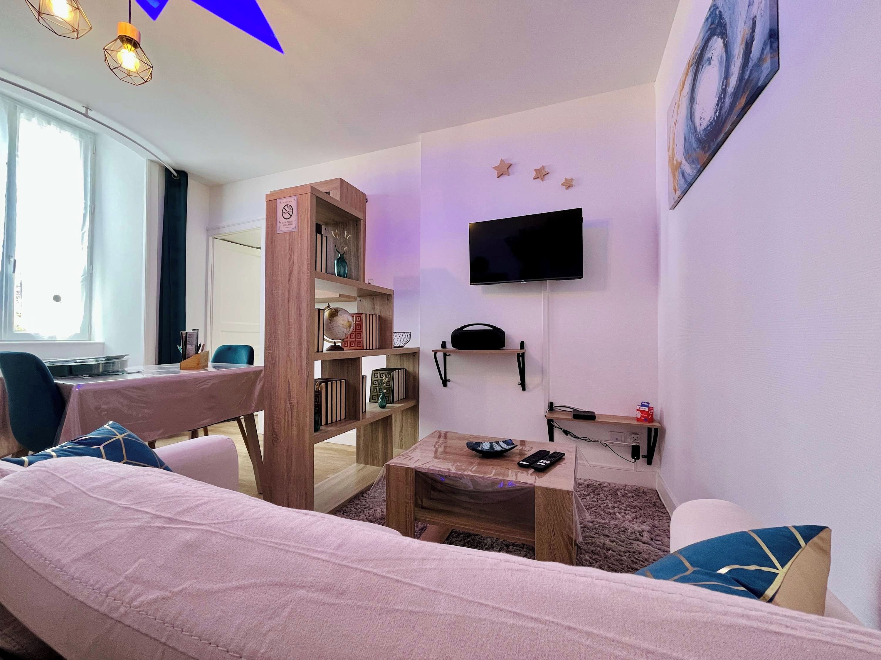 Een woonkamer met een bank, salontafel, boekenkast, een aan de muur bevestigde televisie en een raam met gordijnen.