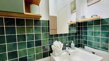 Une salle de bain avec des carreaux verts, un lavabo blanc, un miroir et une étagère contenant des articles de toilette.