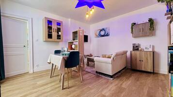 Ein Wohnzimmer mit Essbereich, Holzboden, einer Deckenleuchte und einem an der Wand befestigten Regal mit Pflanzen.