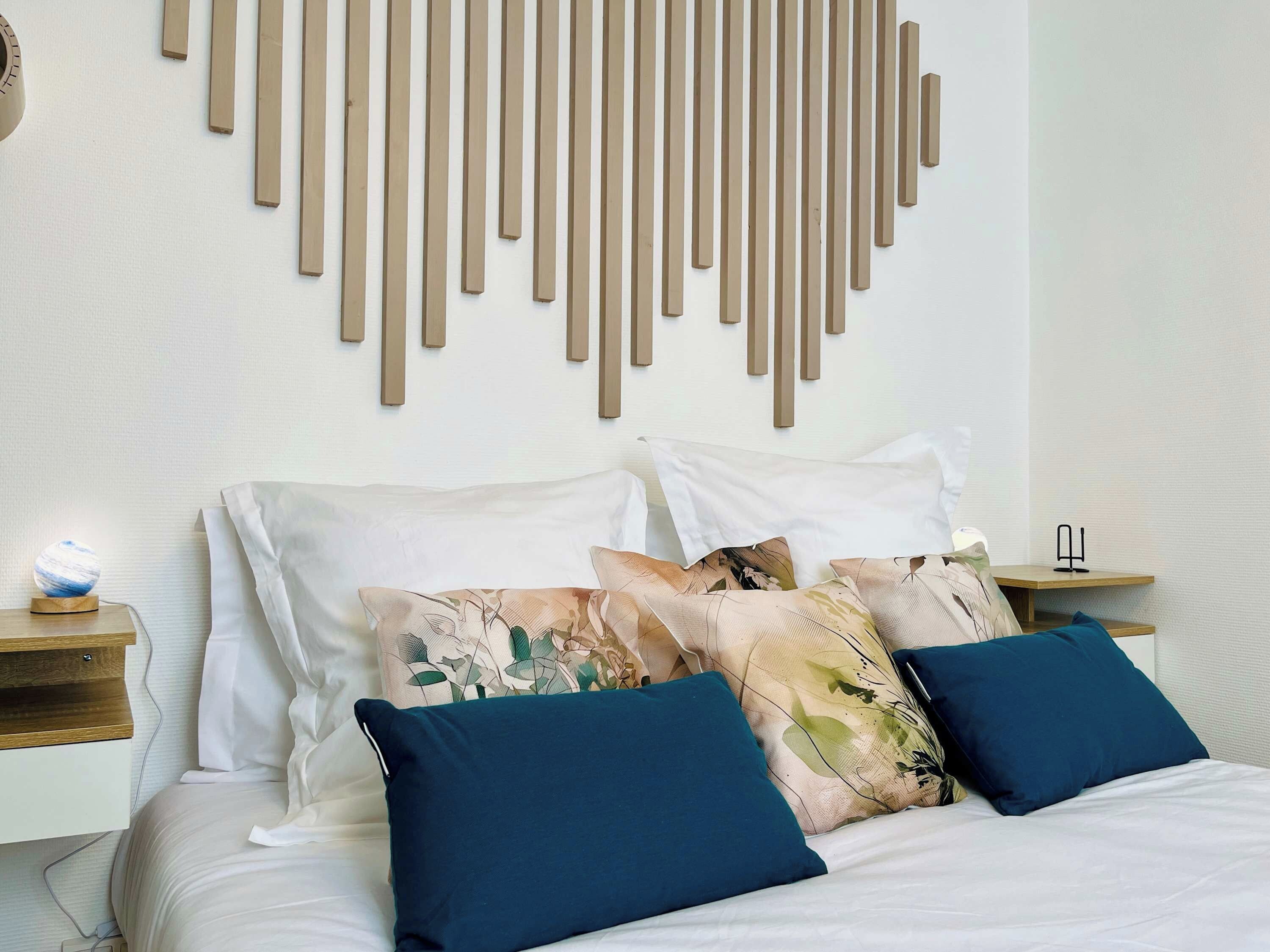 Une chambre à coucher moderne avec un lit, des coussins décoratifs, un luminaire fixé au mur et une table de chevet.