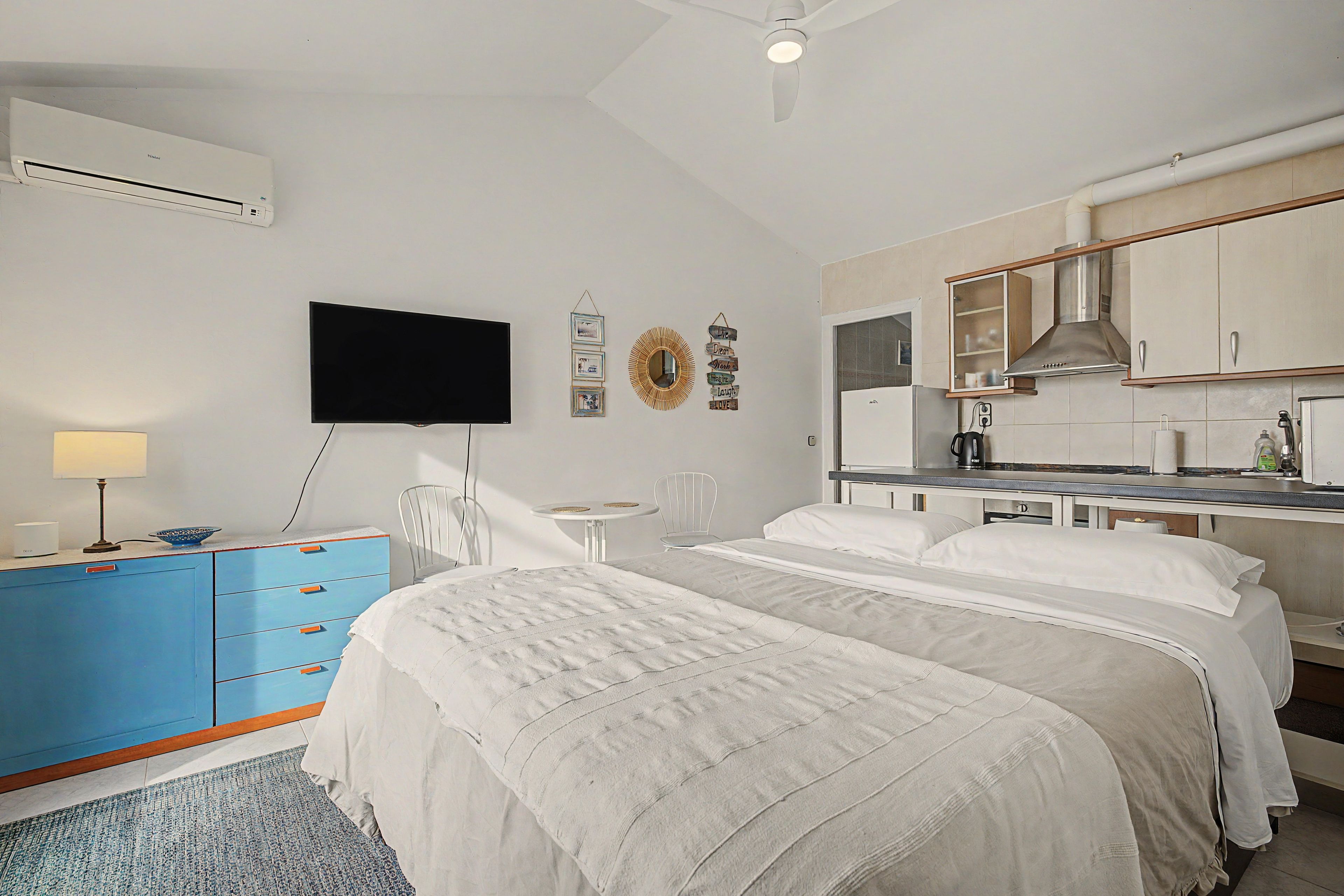 Een slaapkamer met een bed, een bureau, een stoel, een televisie en een kitchenette.